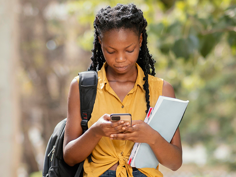Learner checking a mobile device while carrying study materials.